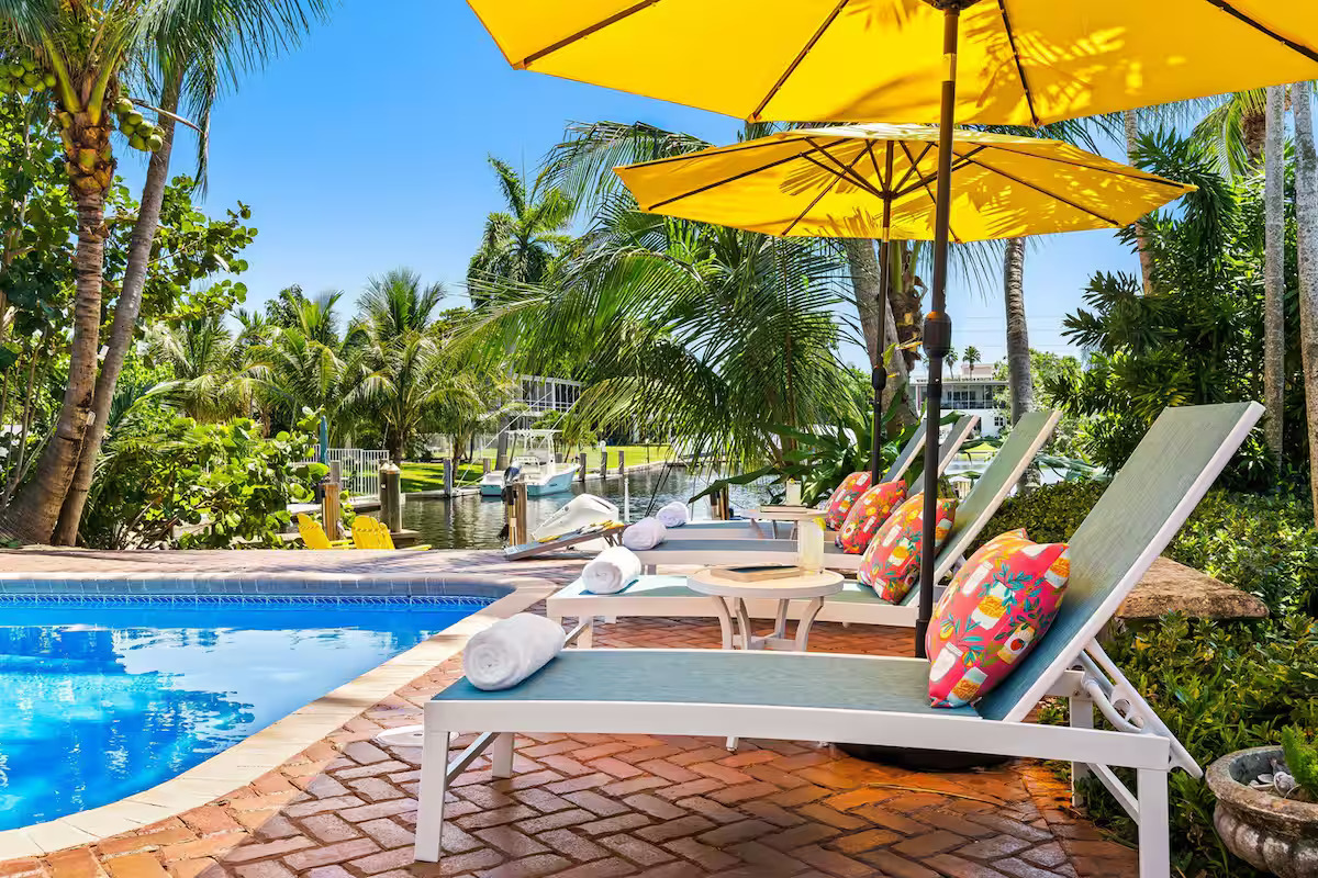 Luxury pool area with lounge chairs, yellow umbrella, palm trees, and waterfront canal views