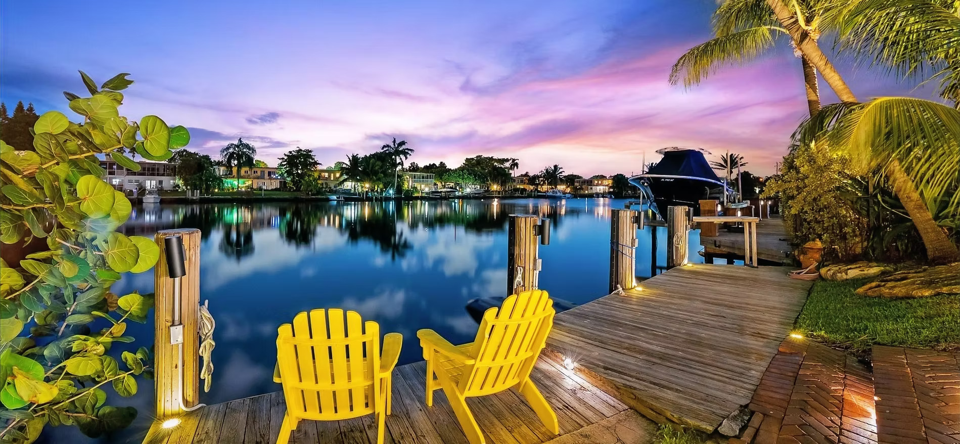 Panoramic twilight view of private dock, yellow Adirondack chairs, and purple sky reflected in the canal