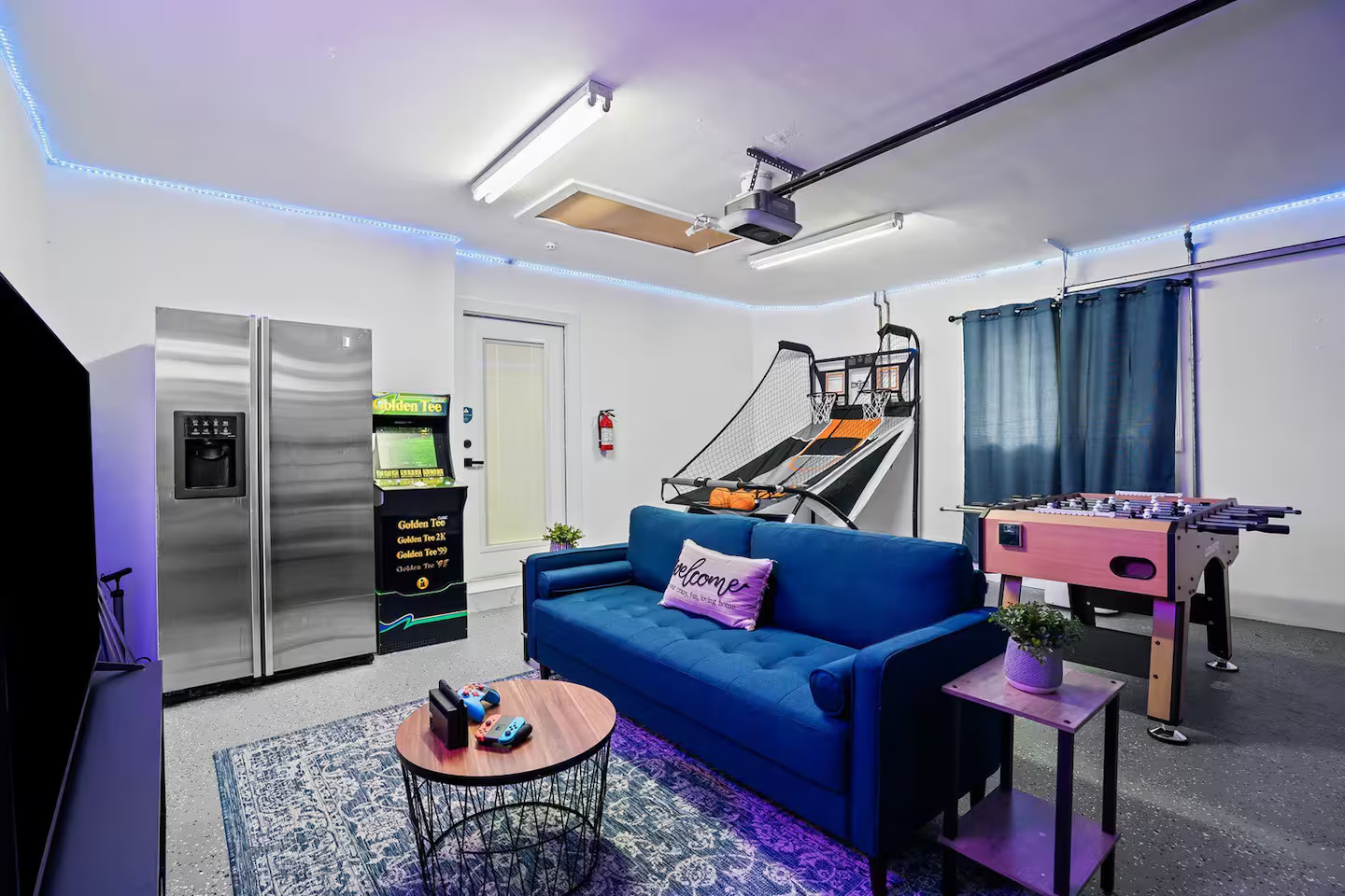 Full game room with Golden Tee arcade machine, foosball table, basketball hoop, and sectional sofa with LED lighting
