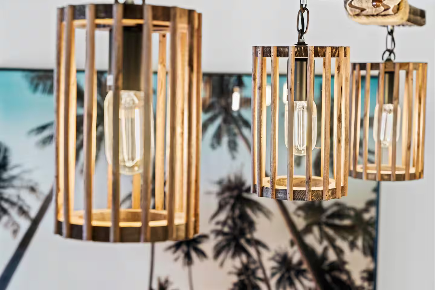 Custom artisan wood-slat Edison bulb pendant lights with tropical palm wall art — interior design detail